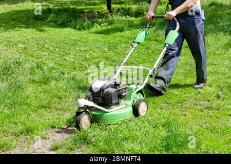 Il lavoratore con un tosaerba a gas tosa il prato in un parco cittadino. Foto Stock