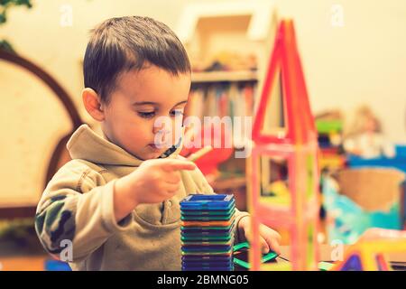 Il ragazzo 2 anni costruire una torre da un costruttore luminoso. Ragazzo sorridente che gioca con il giocattolo costruttore magnetico. Ragazzo che gioca giocattoli intellettuali Foto Stock