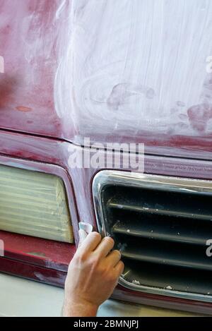 Una vista ravvicinata della mano di un uomo levigando il cofano di un camion prima di un lavoro di verniciatura Foto Stock