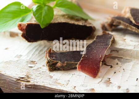 Fette sottili di salsicce di cervo o carne di capra secca servite su una tavola bianca Foto Stock