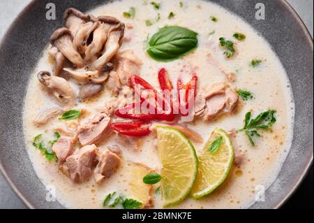 Tom Kha Gai o zuppa di pollo al cocco tailandese in una ciotola grigio opaco sullo sfondo di cemento. Tom Kha Gai è piatto della cucina tailandese con latte di cocco, pollo, gal Foto Stock