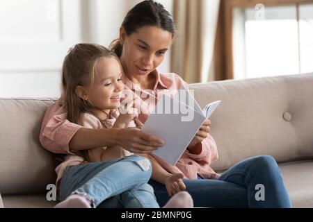 Madre amorevole lettura libro a figlia piccola a casa Foto Stock