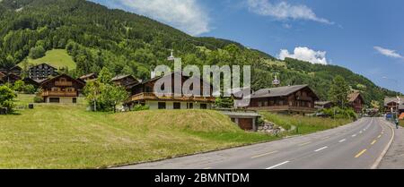 Classico chalet svizzero nel mezzo di verdi prati alpini . Accogliente villaggio rurale Champery in Svizzera. Cielo blu brillante e nuvole bianche e morbide Foto Stock