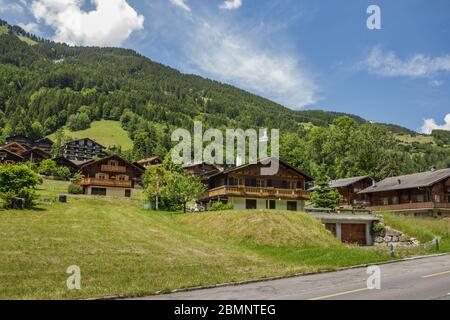 Classico chalet svizzero nel mezzo di verdi prati alpini . Accogliente villaggio rurale Champery in Svizzera. Cielo blu brillante e nuvole bianche e morbide Foto Stock