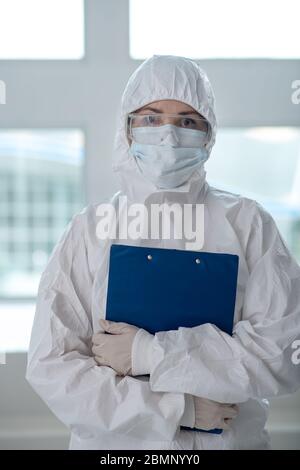 Operatore medico in indumenti protettivi, maschera medica e occhiali di protezione che tengono il fermaglio pieghevole Foto Stock