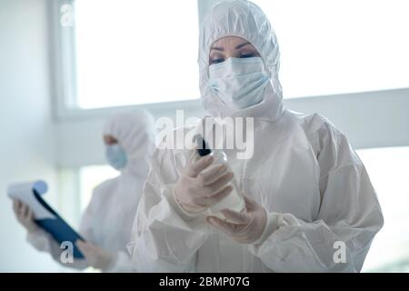 Donna operatrice in indumenti protettivi e maschera medica che tiene antisettico Foto Stock