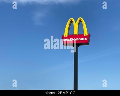 Ashford, Regno Unito - 23 aprile 2020: Primo piano di McDonalds segno all'aperto con la lettera M gialla arrotondata tipica contro il cielo blu. McDonald's è la t Foto Stock