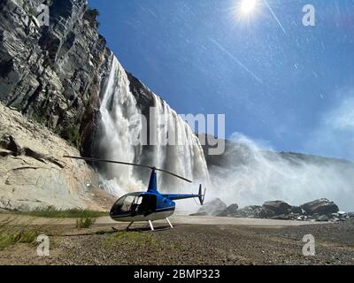 Un pilota ha parcheggiato il suo elicottero sotto una grande cascata. Impressionante quanto acqua scende dall'alto. Foto Stock