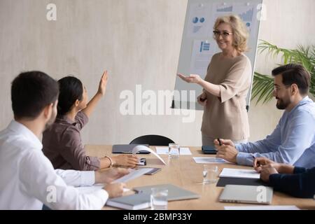 Sorridente donna d'affari indiana che alza la mano chiedendo mentore maturo in sala da consiglio. Foto Stock