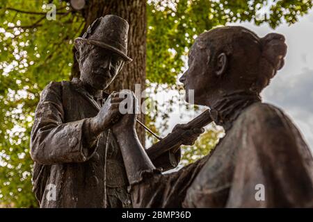 Primo piano della scultura in bronzo di Quirin Roth a Schliersee: i volti dell'uomo in piedi e della donna seduta rivolti l'uno verso l'altro. 16 agosto 2011. Schliersee, circondario di Miesbach, Baviera, 83727, Germania Foto Stock