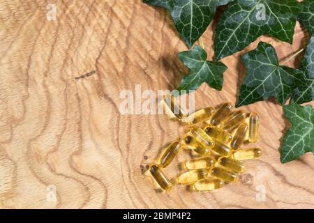 Capsule oblunghe gelatinose trasparenti di olio di pesce sono state sparse sullo sfondo di legno. Acidi grassi polinsaturi Omega-3-essenziali. Spazio di copia Foto Stock