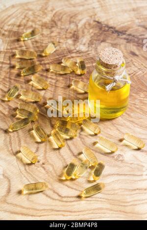 La luce solare dorata brillante splende attraverso una bottiglia di olio vegetale e capsule oblunghe trasparenti con olio di pesce su un legno. Omega-3-essenziale poliunsat Foto Stock