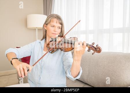 Donna matura che gioca violino nel suo appartamento urbano Foto Stock