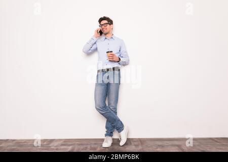 Giovane uomo impegnato a parlare al telefono con una tazza da caffè. Ritratto sicuro, stile di vita moderno, concetto di comunicazione Foto Stock