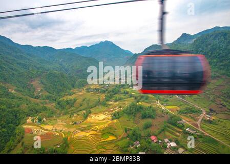 Cabina rossa della funivia che porta alla cima di Phan Xi Păng, passando rapidamente di fronte alla telecamera con movimento sfocato e vista sulla valle SA Pa, SA Pa, vie Foto Stock