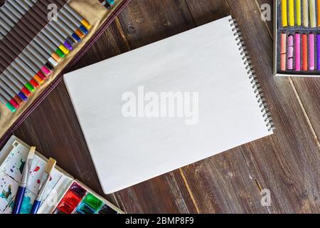 luogo di lavoro artistico, matite, pennelli, vernici acquerello, calchi pastello di carta e pastello. Piatto, tavolo di legno sfondo Foto Stock