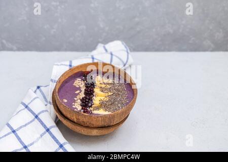 Ciotola di frullato di BlackBerry con banana, chia e semi di girasole in una ciotola di cocco naturale su tavolo grigio neutro con spazio per il testo Foto Stock