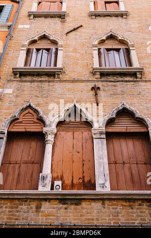 Le finestre di Venezia sono un edificio di più piani, in mattoni rossi, tre finestre con persiane marroni sul fondo, due finestre con persiane in legno Foto Stock