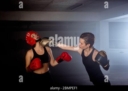 Due pugili professionali femminili che si pugna l'uno con l'altro in combattimento aggressivo del box del garage Foto Stock