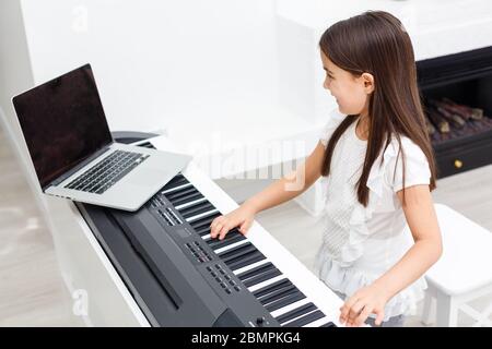 Musicista giovane e grazioso che suona il pianoforte digitale classico a casa durante la lezione online a casa, distanza sociale durante la quarantena, autoisolamento, online Foto Stock