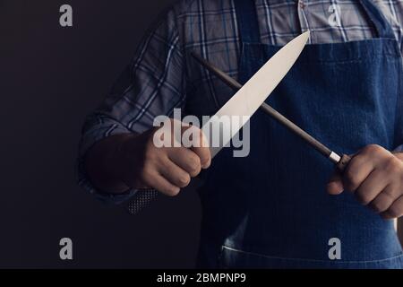 coltello per affilare mani da chef maschio con asta per affilare. Sfondo scuro. Tasto basso Foto Stock