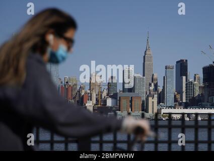 Hoboken, Stati Uniti. 10 maggio 2020. Una donna indossa una maschera protettiva mentre scherza a Hoboken, New Jersey, con una vista dell'Empire state Building e dello skyline di Manhattan domenica 10 maggio 2020. La pandemia di Coronavirus ha ucciso 20,000 persone a New York City e oltre 270, 00 morti in tutto il mondo. Foto di John Angelillo/UPI Credit: UPI/Alamy Live News Foto Stock