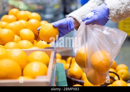 Donna mani in guanti medici sceglie arance fresche pieghevole in un sacchetto di plastica monouso in supermercato, primo piano. Misure di protezione contro i coronavi Foto Stock