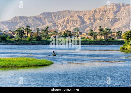 Il pescatore sul fiume Nilo trasporta nella sua cattura con le montagne della sponda occidentale del Nilo sullo sfondo Foto Stock