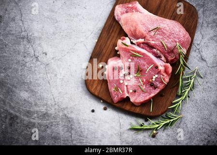 Carne di maiale cruda su tagliere di legno al tavolo da cucina per cucinare bistecca di maiale arrosto o grigliato con ingredienti erbe e spezie, maiale fresco Foto Stock