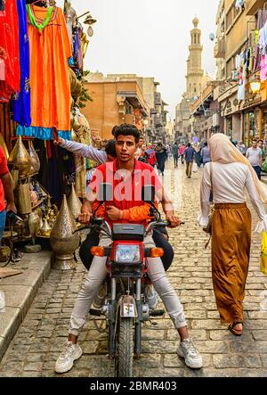 Tre giovani uomini in moto che percorrono al Muizz Street, salutando gli amici lungo il tragitto Foto Stock