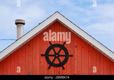 La baracca del pescatore façade. Ruota della nave nera su un bordo dipinto di rosso. Fascia bianca a tegola contro un cielo blu nuvoloso. North rustico Harbour, PEI Canada Foto Stock