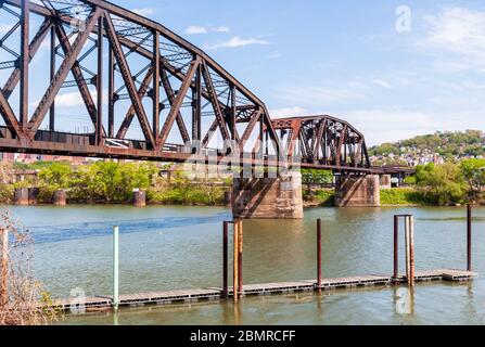 Un molo vuoto lungo il fiume Allegheny sotto un vecchio ponte ferroviario in una giornata di sole primavera, Pittsburgh, Pennsylvania, USA Foto Stock