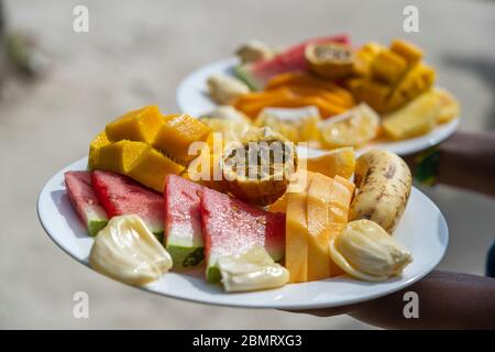 Frutta tropicale su un piatto da colazione, primo piano. Anguria fresca, banana, frutto della passione, ananas, jackfruit, mango, papaya, arancia per mangiare in bea Foto Stock