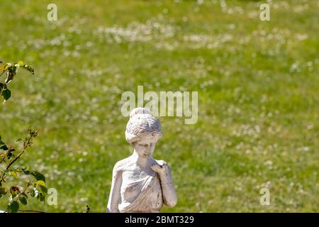 Fuoco selettivo su una vecchia figura di calcare di tempo di una donna nel giardino davanti ad un prato sfocato con daisie ad una giornata di sole. Fotografia macro Foto Stock