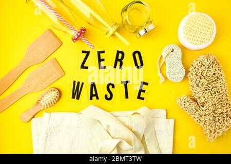 Concetto di zero sprechi. Sacchetti eco in tessuto, vasetti in vetro, spazzola e panno in legno per capelli e su sfondo giallo con testo nero Zero Waste al centro. Foto Stock