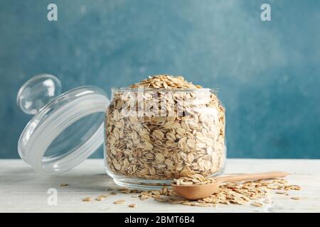 Vaso di vetro con farinata d'avena e cucchiaio su tavolo di legno bianco Foto Stock