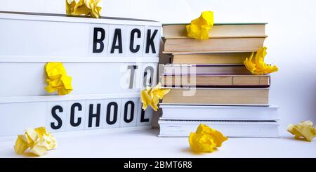 Scatola luminosa con testo DI RITORNO A SCUOLA e libri su sfondo bianco con carta gialla sbriciolata Foto Stock