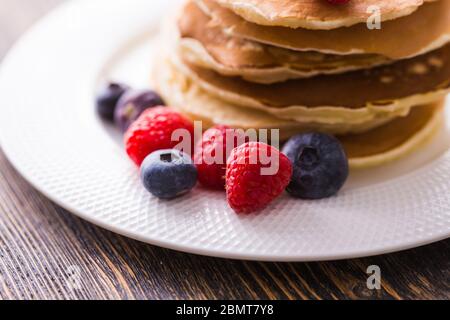 Mucchio di pancake con mirtilli e lamponi per colazione su tavolo di legno. Foto Stock