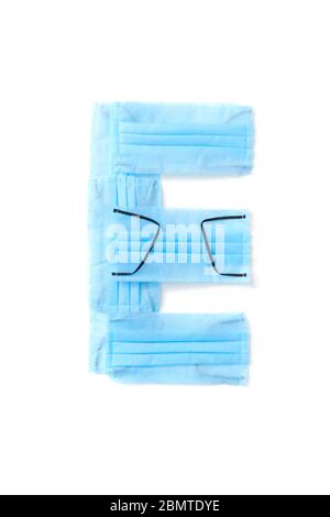 Lettera e realizzata con maschere mediche protettive su sfondo bianco. Foto Stock