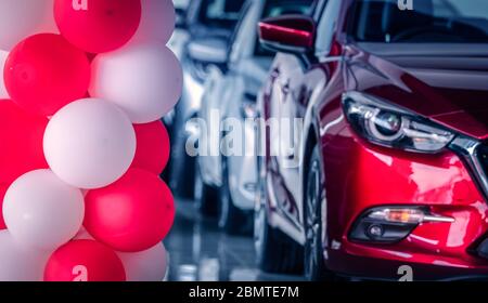 Palloncini rossi e bianchi decorati in uno showroom di auto moderne su una vettura SUV rossa con vista frontale sfocata. Nuova e luminosa auto SUV di lusso parcheggiata in uno showroom moderno. Foto Stock