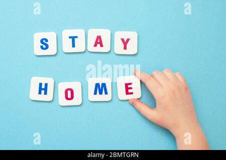 Vista superiore della mano del bambino che fa con le lettere la parola soggiorno a casa su sfondo blu. La creatività dei bambini in quarantena. Foto Stock