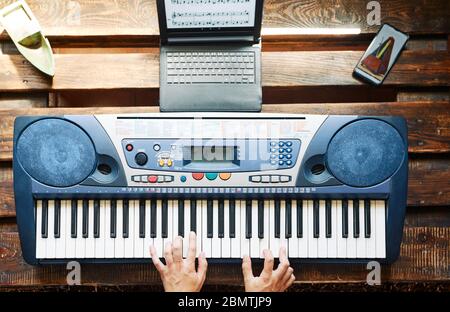 Uomo che suona il pianoforte mentre prende le lezioni in linea a casa ed usando un metronomo Foto Stock