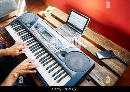 Un uomo che suona il pianoforte a casa mentre usa un tablet per leggere i punteggi Foto Stock