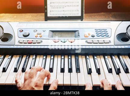 Uomo che suona il pianoforte a casa mentre usa un tablet per leggere i punteggi Foto Stock