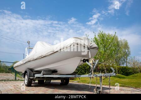 Grande nave gommone moderna coperta con protezione grigio o bianco tarp in piedi su semirimorchio in acciaio a casa cortile in giorno di sole luminoso Foto Stock