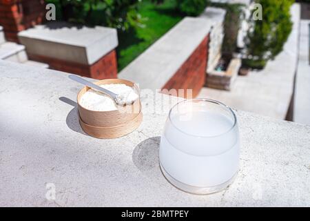 Collagene con cucchiaio e bicchiere d'acqua su fondo in cemento. Concetto di salute e bellezza alla moda. Foto Stock