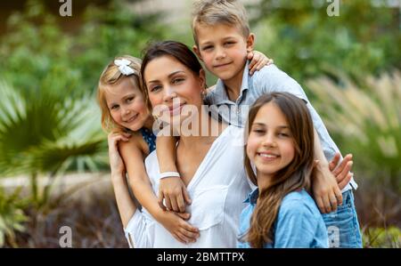 Ritratto di una bella giovane madre con piacere passare il tempo con i suoi tre bambini preziosi nel parco primaverile, divertirsi insieme, grande famiglia felice Foto Stock