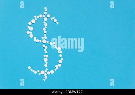 Pillole bianche in forma di simbolo del dollaro su sfondo blu. Concetto farmaceutico di spese mediche e prezzi per la medicina, il farmaco o la malattia curme Foto Stock