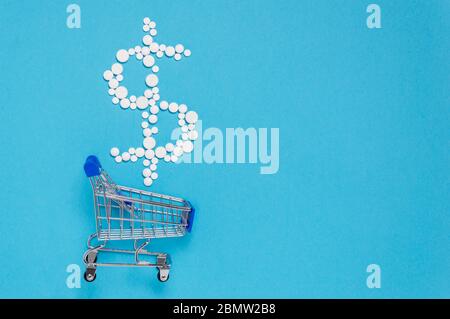 Pillole bianche in forma di segno del dollaro sopra il carrello di shopping su sfondo blu. Concetto farmaceutico di spese mediche e prezzi per la medicina, farmaci Foto Stock