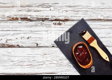 Salsa barbecue in una ciotola di legno con spazzola sopra un tavolo di legno rustico bianco / sfondo con spazio libero per il testo immagine ripresa dalla vista dall'alto. Foto Stock